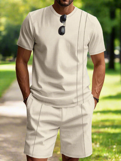 Man wearing a beige shorts set with sunglasses on a white background
